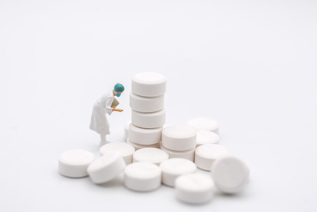 Foto gezondheidszorg en medisch concept closeup van vrouwelijke arts miniatuur figuur met patiënt dossier op zoek naar stapel witte pillen op witte achtergrond