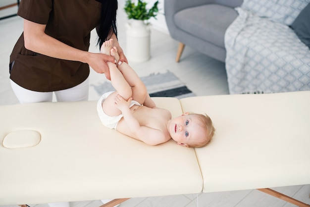 Gezondheidszorg en medisch concept. Een professionele vrouwelijke masseuse maakt een massage en gymnastiek voor een kleine baby in een moderne, gezellige kamer.