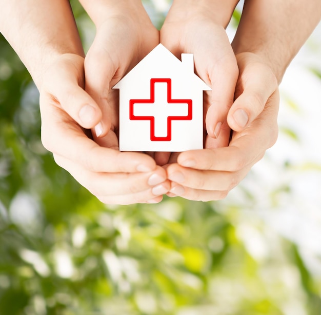 gezondheidszorg, geneeskunde en liefdadigheidsconcept - mannelijke en vrouwelijke handen die Witboekhuis met rood kruisteken houden