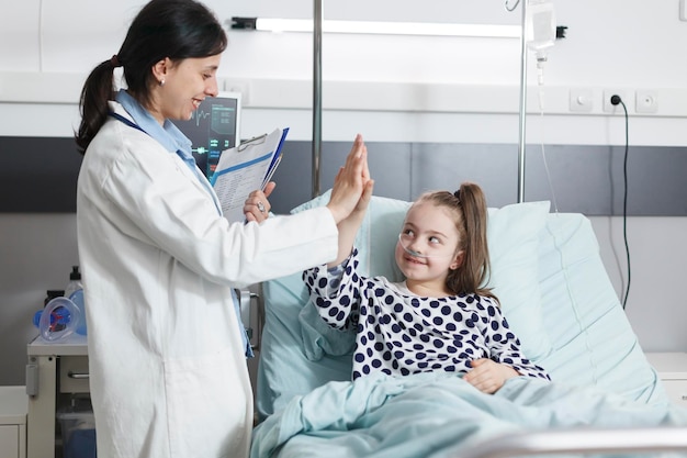 Gezondheidszorg kliniek kinderarts expert high-fiving ziek klein meisje terwijl in de patiënt recovery ward kamer.