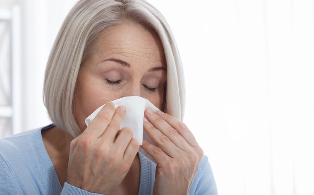 Gezondheidszorg, koude, allergie en zieke vrouw blaast haar loopneus in papieren zakdoekje.