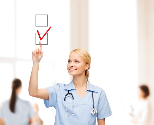 gezondheidszorg, medisch en technologie - jonge arts of verpleegster met een markering die een rood vinkje trekt in het selectievakje met team op de achterkant