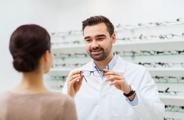 gezondheidszorg, mensen, gezichtsvermogen en visieconcept - opticien die bril toont aan vrouw in optiekwinkel