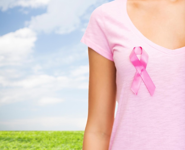 gezondheidszorg, mensen, liefdadigheid en geneeskunde concept - close-up van vrouw in t-shirt met roze borstkanker bewustzijn lint over blauwe lucht en gras achtergrond