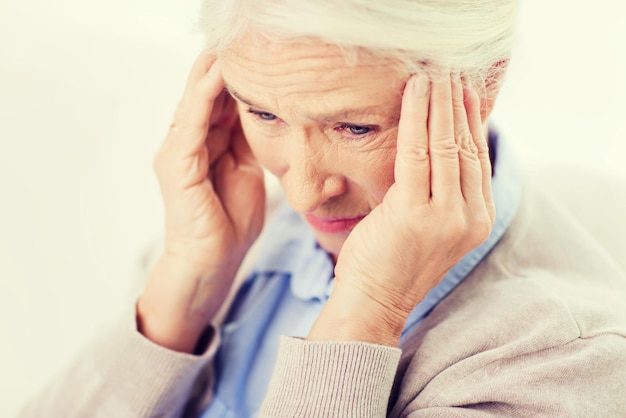 gezondheidszorg, pijn, stress, leeftijd en mensenconcept - gezicht van senior vrouw die aan hoofdpijn lijdt