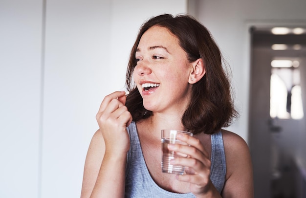 Gezondheidszorgmedicatie en vrouw die een pil drinkt met een glas water voor wellness bij haar thuis Geneeskunde medische en gelukkige vrouwelijke persoon die een vitaminesupplement of tablet met vloeistof in appartement neemt