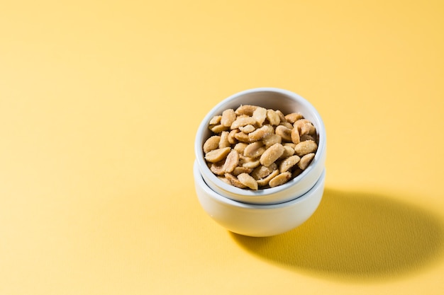 Gezouten pinda's in een witte kom op een delt-achtergrond in hard licht. Gezond modern vegetarisch eten.