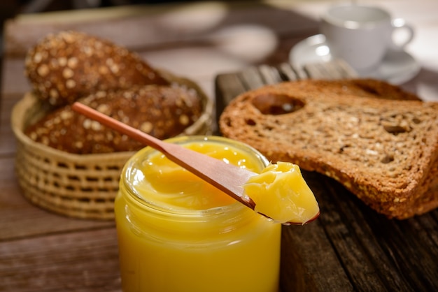 Ghee butter in glass jar with wooden spatula and sliced bread on wooden table