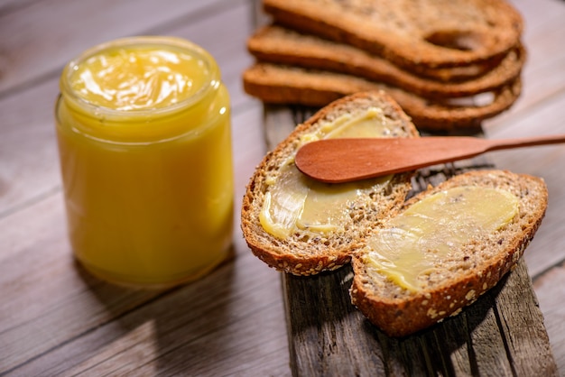 Photo ghee butter in glass jar with wooden spatula and sliced bread on wooden table