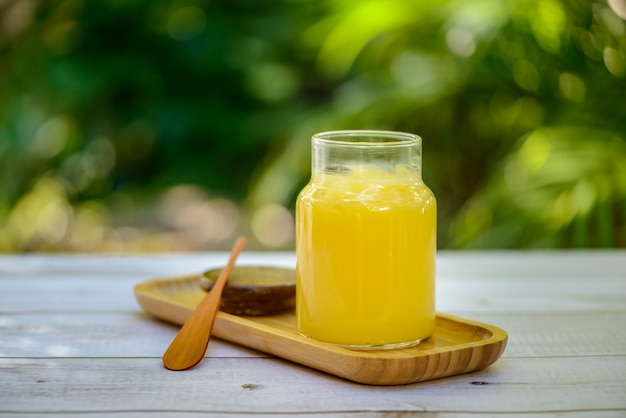 Ghee butter in glass jar with wooden spatula on white wooden table with blurred green background.