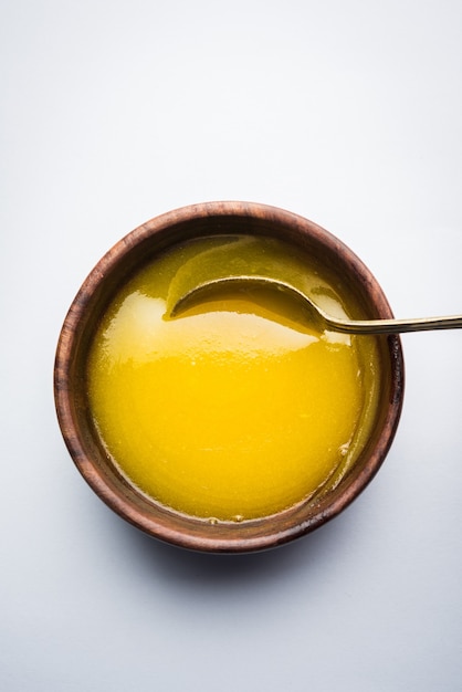 Ghee or clarified butter close up in wooden bowl and silver spoon, selective focus