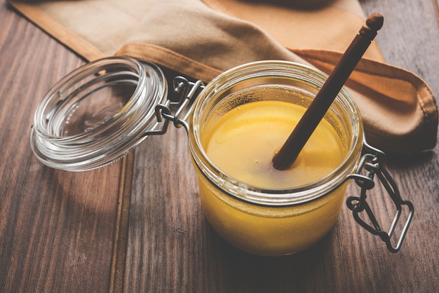 Ghee or clarified butter close up in wooden bowl and silver spoon, selective focus