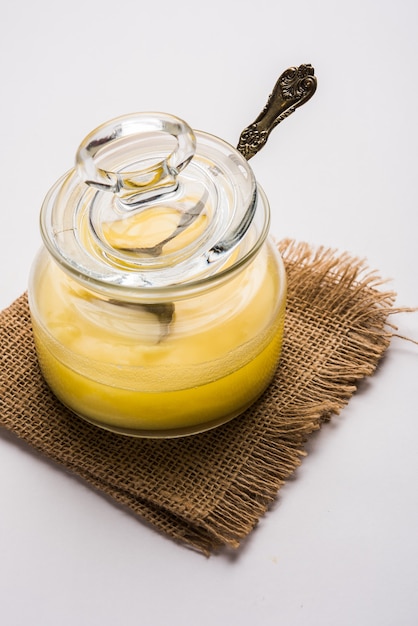 Ghee or clarified butter close up in wooden bowl and silver spoon, selective focus