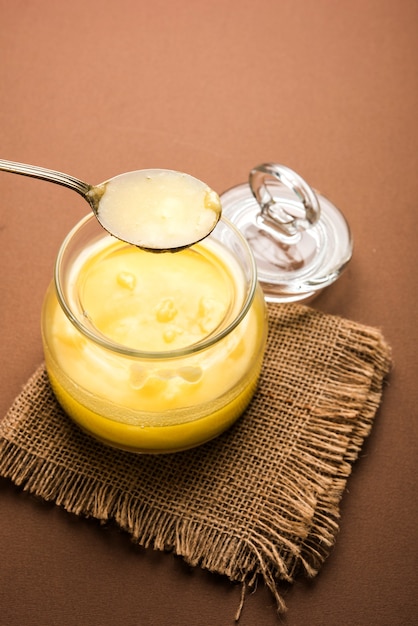 Photo ghee or clarified butter close up in wooden bowl and silver spoon, selective focus