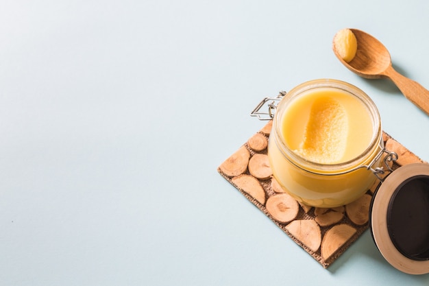 Ghee or clarified butter in jar and wooden spoon on blue background. Top view. Copyspace. Ghee butter have healthy fat and is a common cooking ingredient in many of the Indian food