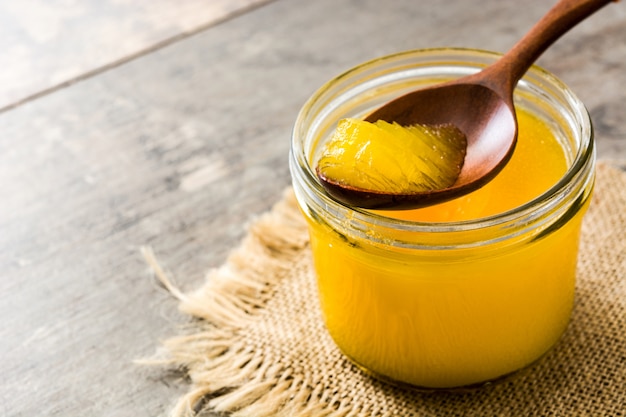 Ghee or clarified butter in jar and wooden spoon on wooden table.