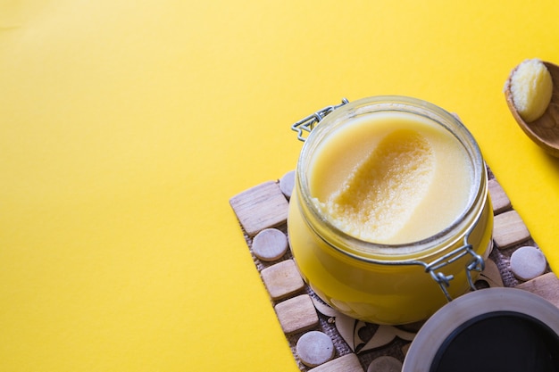 Ghee or clarified butter in jar and wooden spoon on yellow background. Top view. Copyspace. Ghee butter have healthy fat and is a common cooking ingredient in many of the Indian food