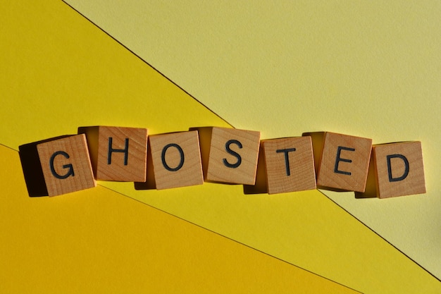 Ghosted word in wooden alphabet letters isolated on yellow background meaning to stop communicating with someone out of the blue