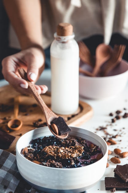 Giet granola uit een pot in een keramische kom terwijl je een granola-smoothie maakt