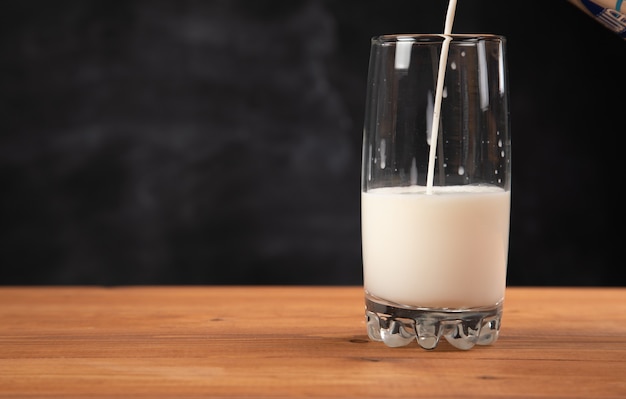 Giet melk in een glas op een houten tafel