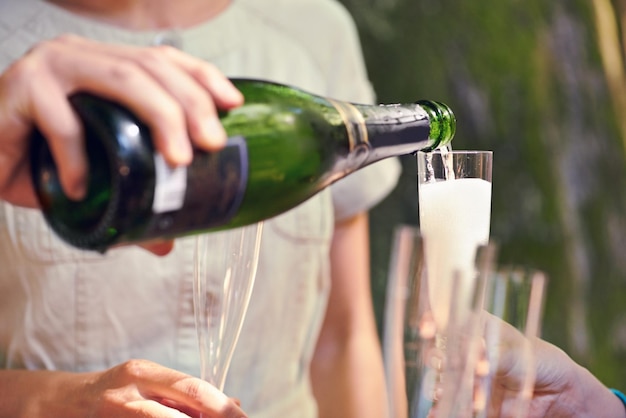 Giet met de hand champagne en glazen voor een groep vrienden voor feestelijke toast en feest in parktuin of natuur Fles mousserende wijn en glas om te vieren voor team van mensen verjaardag of evenement