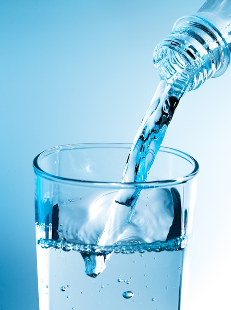 Giet water uit fles in glas met blauw licht