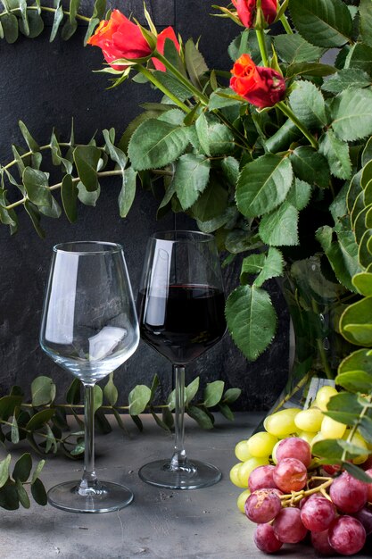 giet wijn uit een fles in een glas, op een zwarte achtergrond met rode rozen en druiven