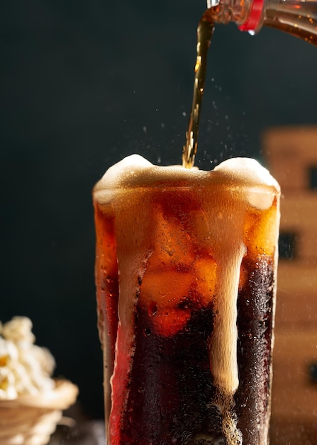 Gieten van cola frisdrank in glas op houten tafel met popcorn