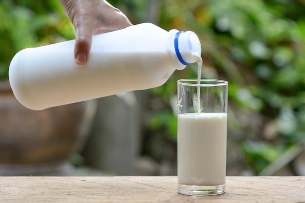 Gieten van melk in het glas met de groene natuur achtergrond.