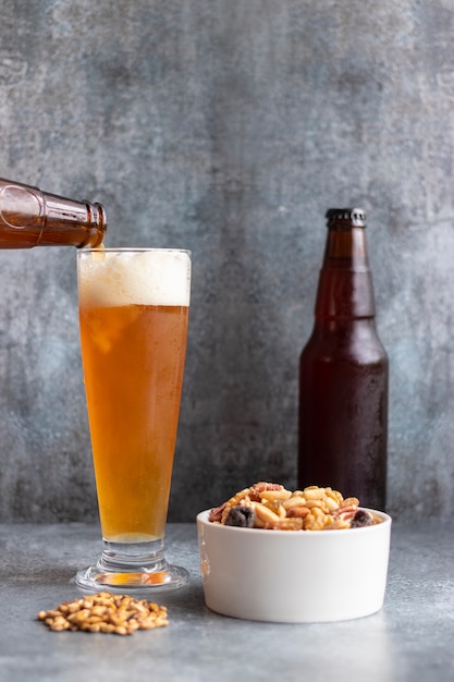 Gietend bier van fles in glas op grijze backgroung