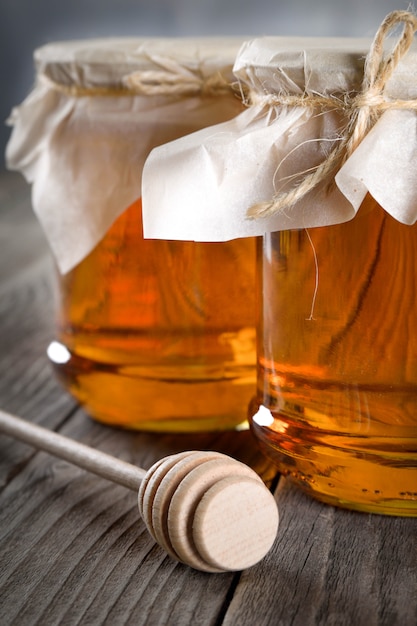 Gietende aromatische honing in kruik, close-up. Honing in glazen potten en honingraten wax op houten tafel.