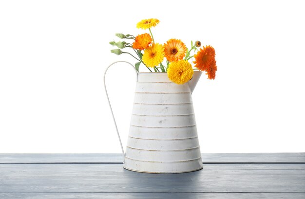 Gieter met bloemen op tafel tegen witte muur