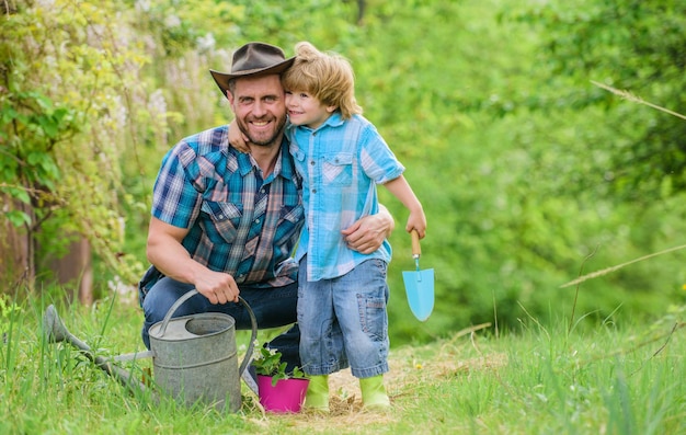 Gieter pot en schoffel Tuingereedschap vader en zoon in cowboyhoed op ranch Eco-boerderij happy earth day Stamboomverzorging klein jongenskind help vader in de landbouw Werken voor jou comfort