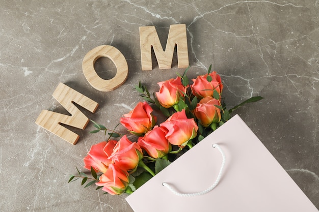 Gift bag with bouquet of orange roses and inscription mom on brown table, top view