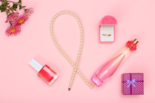 Photo gift box, beads, bottle of perfume, nail polish and golden ring in box on a pink background. women cosmetics and accessories. top view.