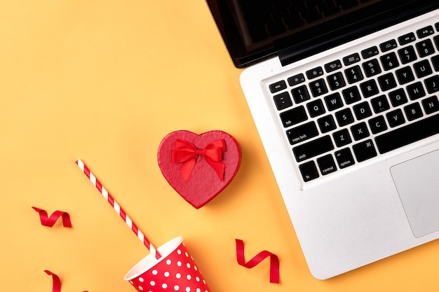 Gift box, birthday party things and laptop on a yellow background