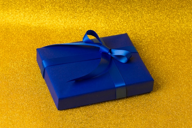 Gift box in blue wrapping paper on a beautiful abstract\
golden
