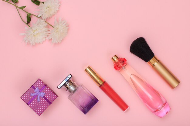 Gift box, bottles of perfume, brush and flowers on a pink background. Women cosmetics and accessories. Top view.