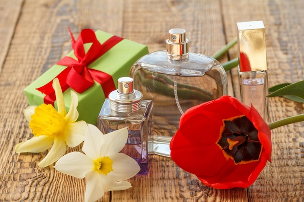 Confezione regalo e bottiglie di profumo su tavole di legno con bouquet di tulipano rosso e narcisi gialli