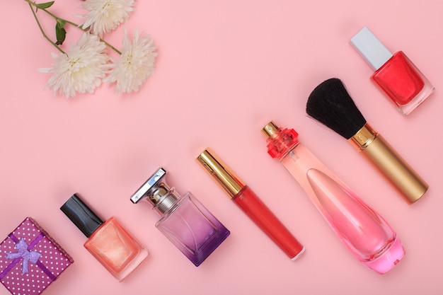 gift box, bottles with nail polish, perfume, brush, lipstick and flowers on a pink background. women cosmetics and accessories. top view.