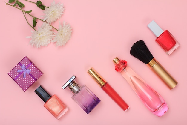 gift box, bottles with nail polish, perfume, brush, lipstick and flowers on a pink background. women cosmetics and accessories. top view.