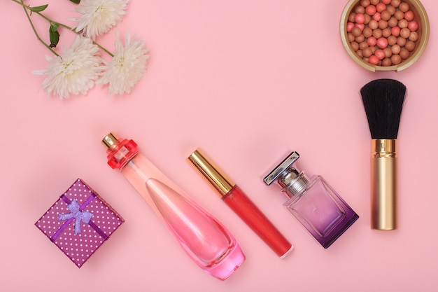 Gift box, bottles with perfume, lipstick, brush and powder on a pink background. Women cosmetics and accessories. Top view.