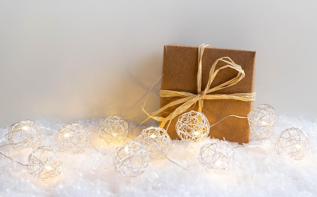 Подарочная коробка и рождественские огни в снегу на белом фоне с копировальным пространством, рождеством и новогодним праздником