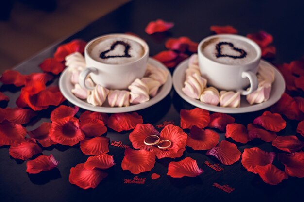 Gift box and coffee cup with wedding rings on rose petals