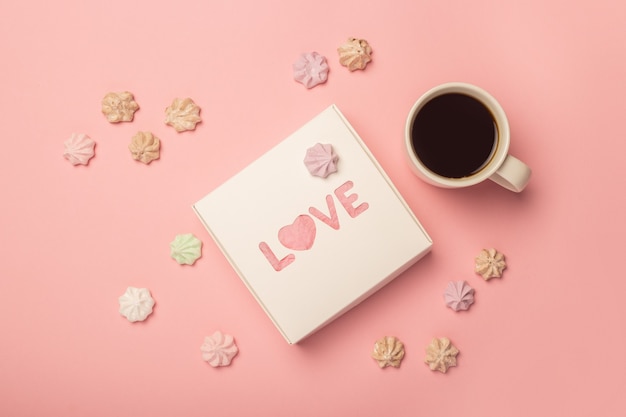 Gift box, cup with coffee and meringues on a pink surface