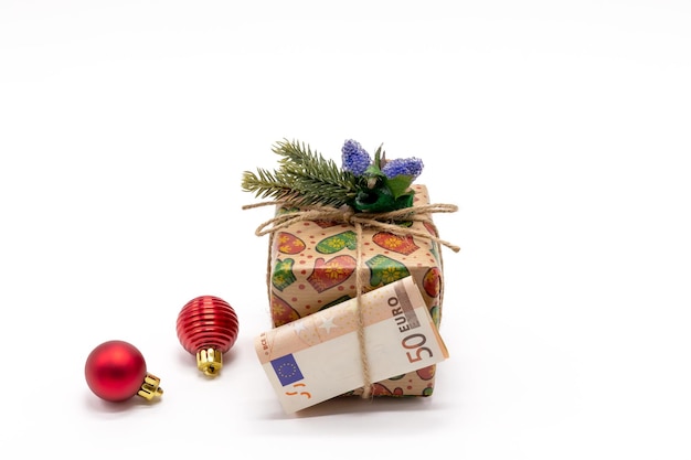 A gift box decorated with a fir branch and a 50 euro paper bill and Christmas tree toys