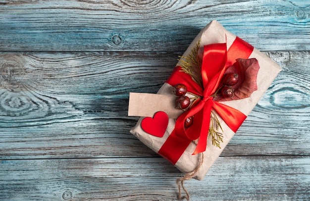 Gift box decorated with a red ribbon, berries and a heart on a natural gray-blue wooden background.