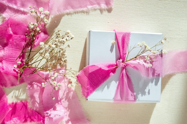 Photo gift box decoration with pink ribbon and dry flowers flat lay