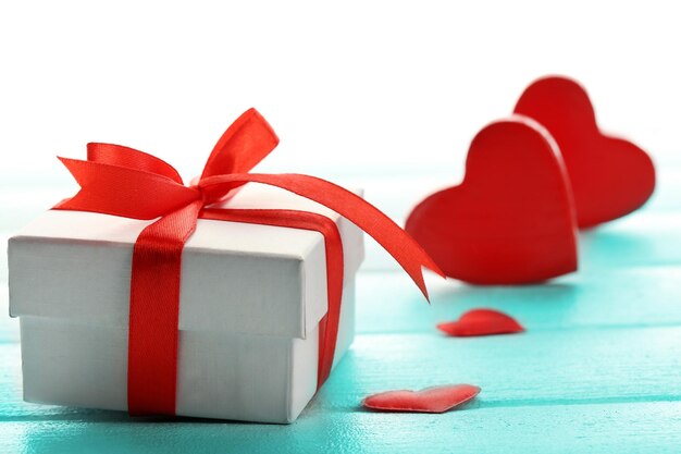 Gift box and decorative hearts on color wooden background