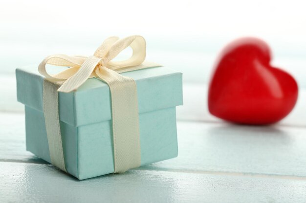 Gift box and decorative hearts on color wooden table on light background